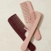 Three wide-tooth combs in blush and burgundy on pale stone.